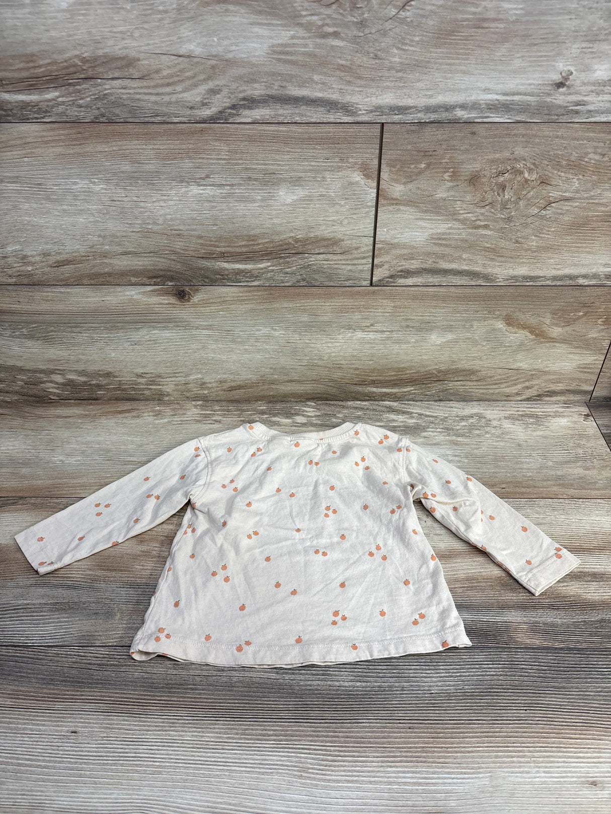 White long-sleeve toddler shirt with small orange fruit pattern laid flat on wooden floor