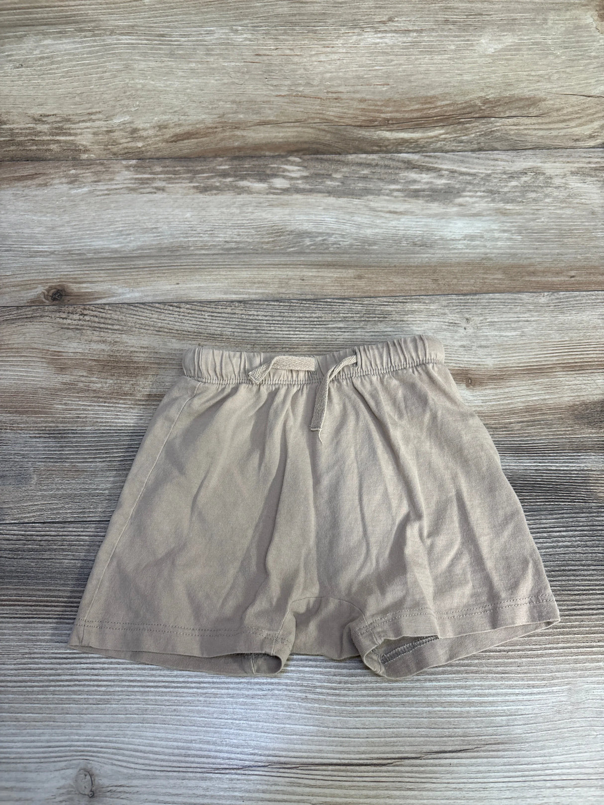Flat lay of beige H&M toddler pull-on shorts showcasing elastic waistband and drawstring with light wood background