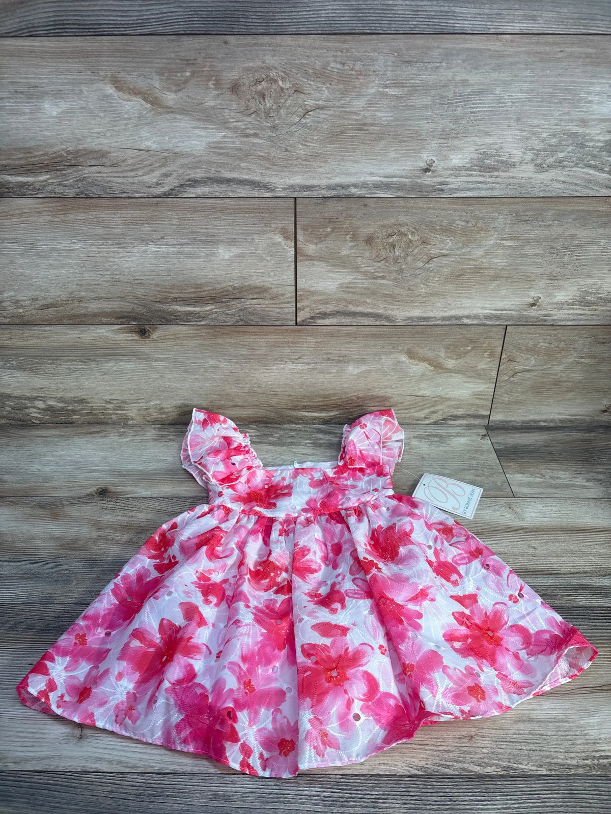 Front view of B by Bonnie Jean toddler dress showcasing pink floral embroidery and ruffled sleeves on a wood surface