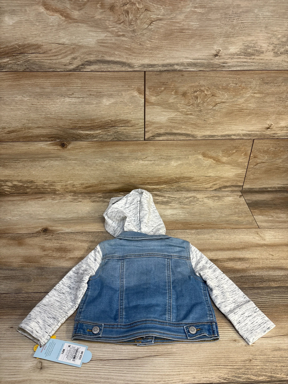 Kids' denim jacket with gray hood and sleeves displayed on wood floor