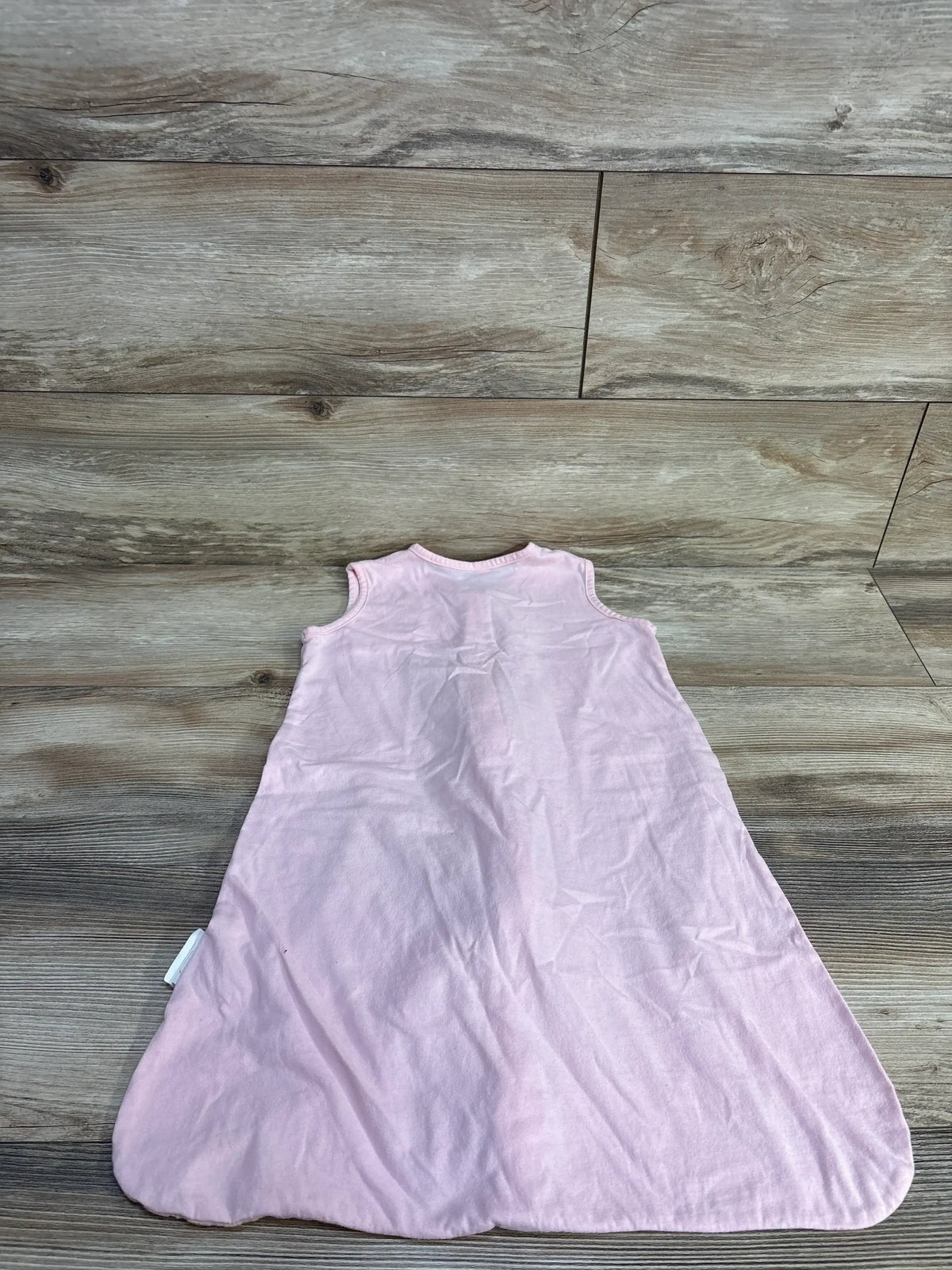 Back view of pink Tillyou sleep sack showcasing sleeveless A line shape and fabric tag laid flat on wood background