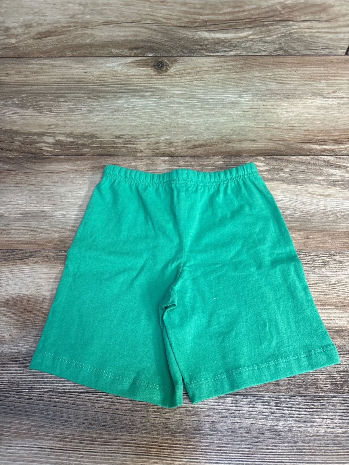 Bright green kids shorts with elastic waist, laid flat on wood floor