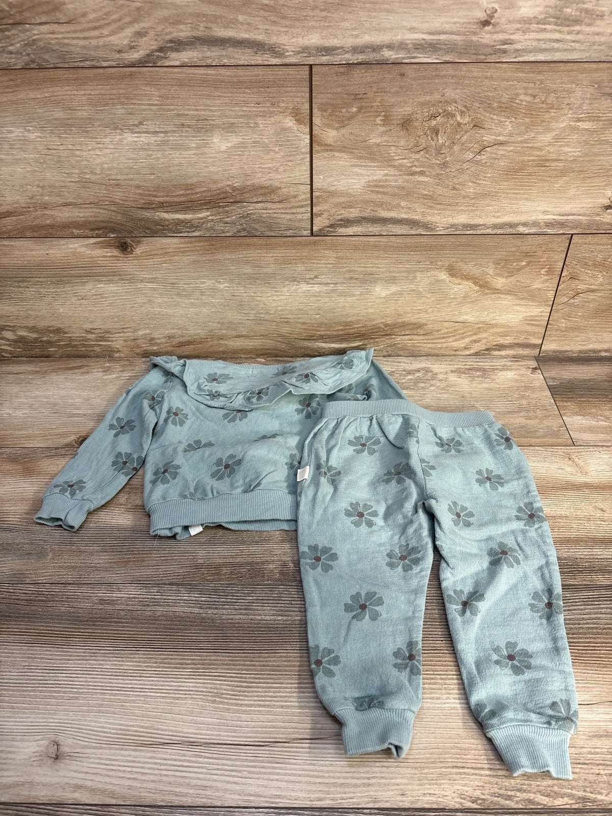 Flat lay of Rabbit + Bear organic cotton 2pc ruffle sweatshirt and pants set in green with floral print on wood