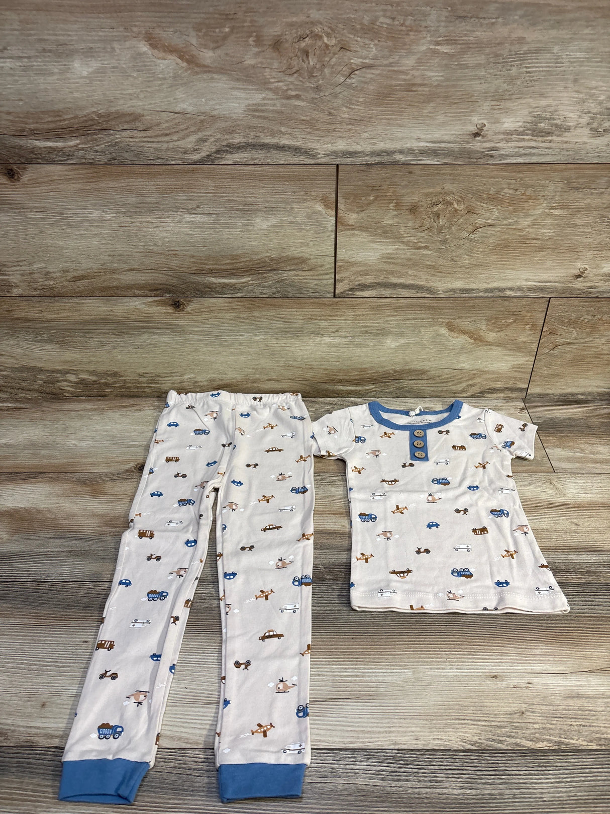 Flat lay of Chick Pea 2-piece pajama set size 4T in beige with blue trim, button placket and elastic waist on wood background