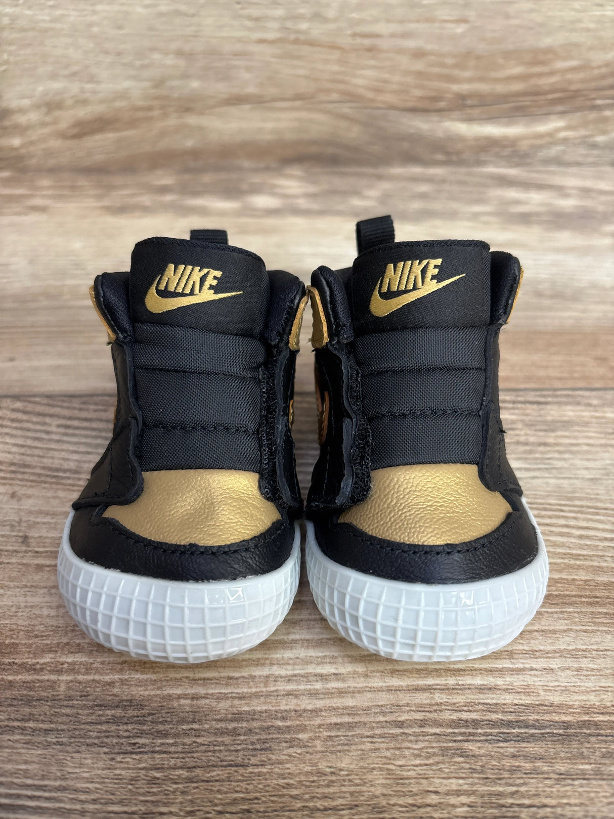 Pair of black and gold Nike baby shoes with white soles on wooden surface