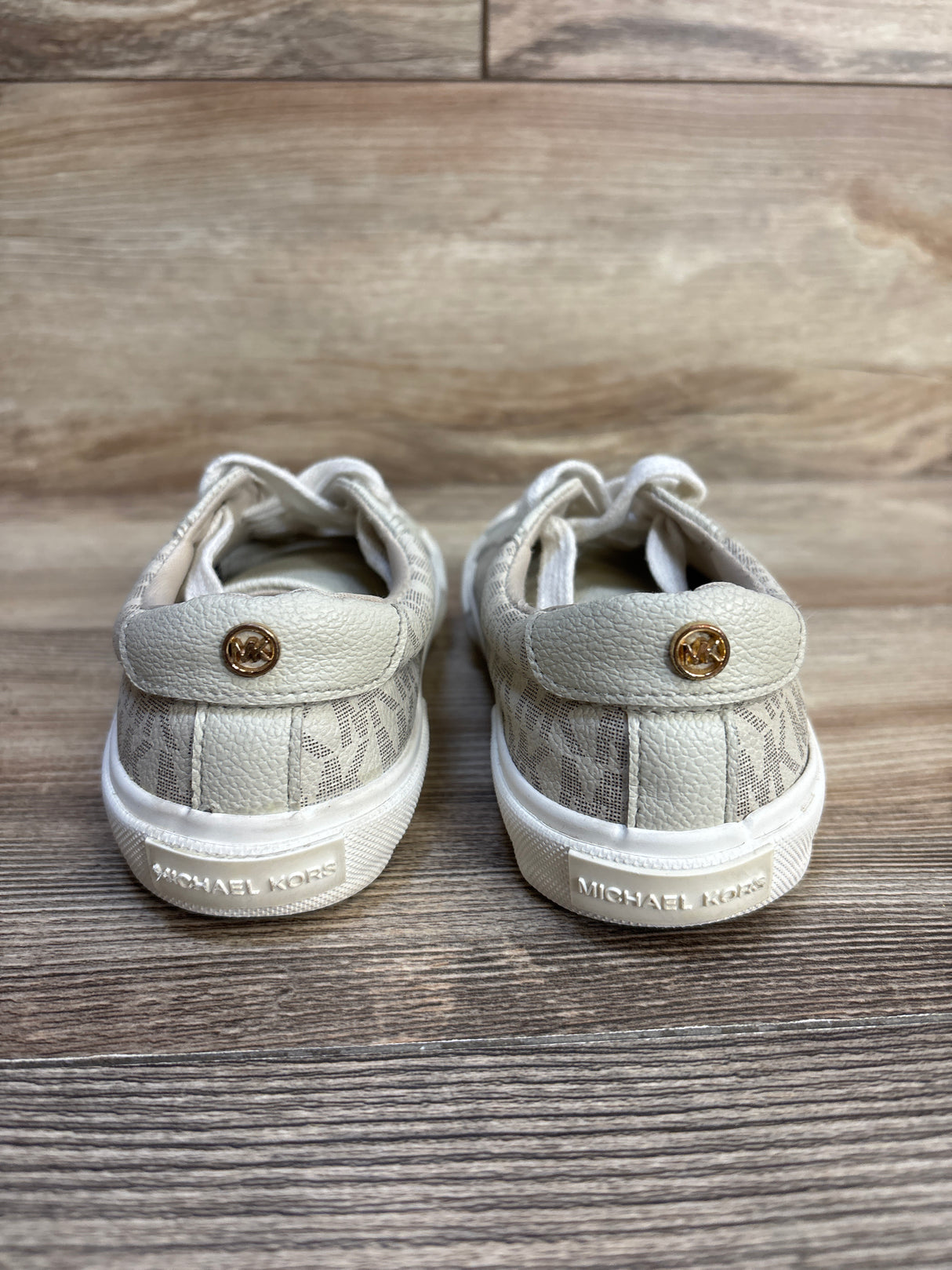 Michael Kors toddler sneakers with gold logo, white soles, and patterned fabric on wood floor
