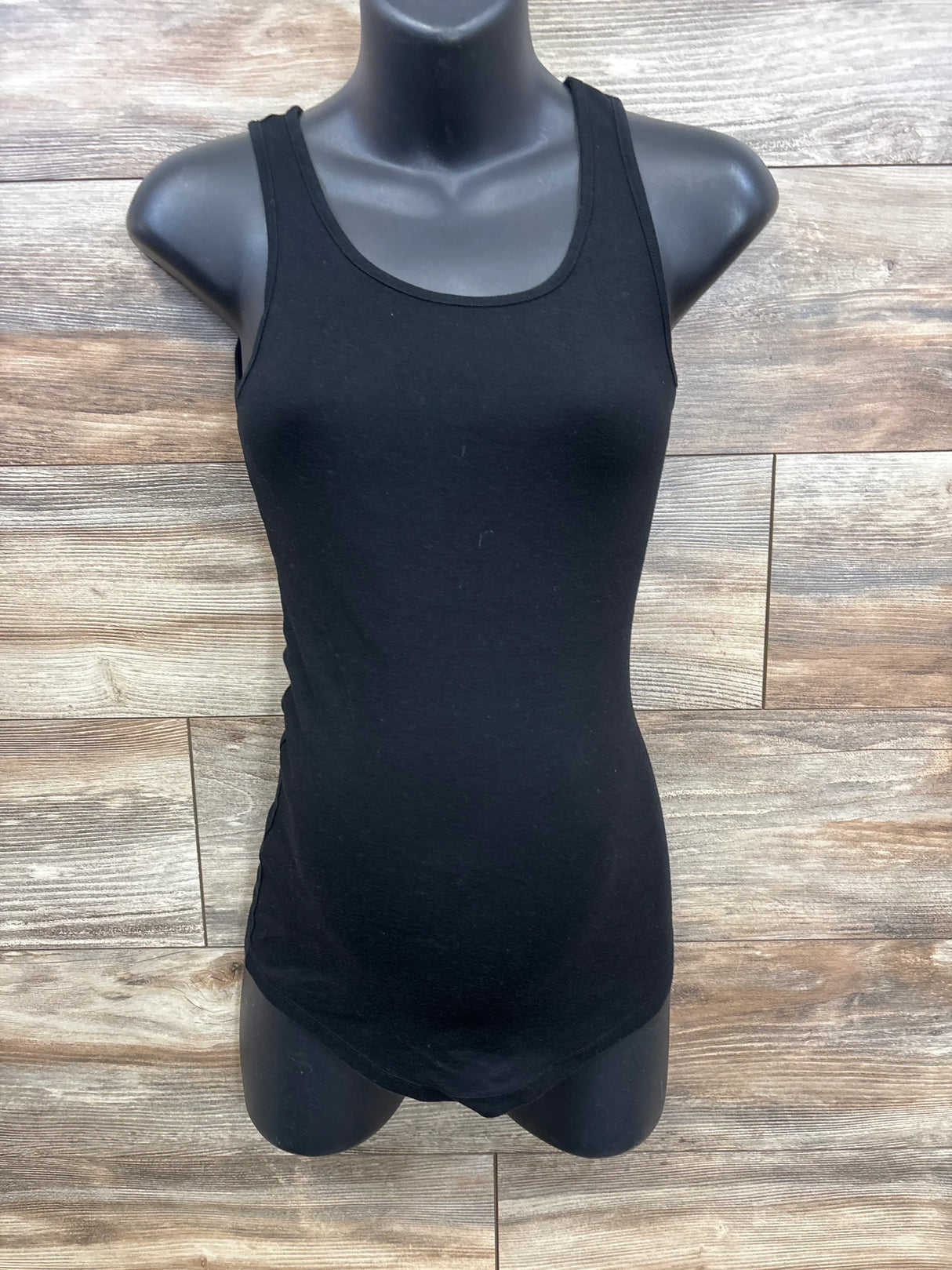 Black sleeveless maternity bodysuit on black mannequin against wooden panel background