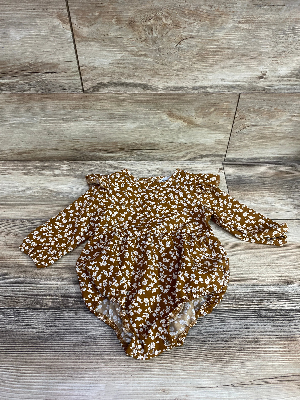 Top-down view of Bailey’s Blossoms long sleeve bubble romper showcasing brown floral print and ruffled shoulders on a wood floor