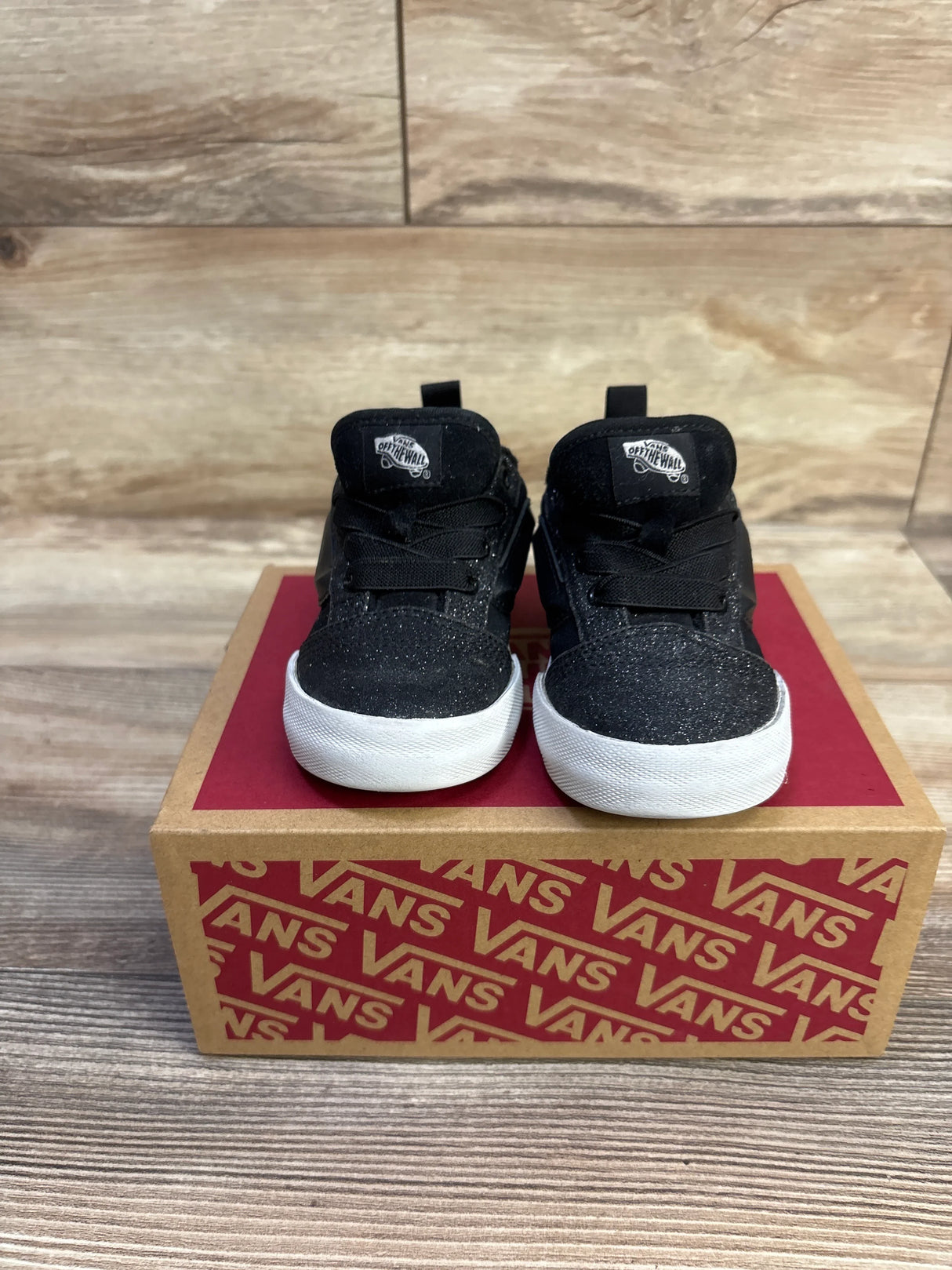 Front view of toddler Vans Knu Skool dazzled black sneakers with glittered upper and white rubber soles on a red Vans box