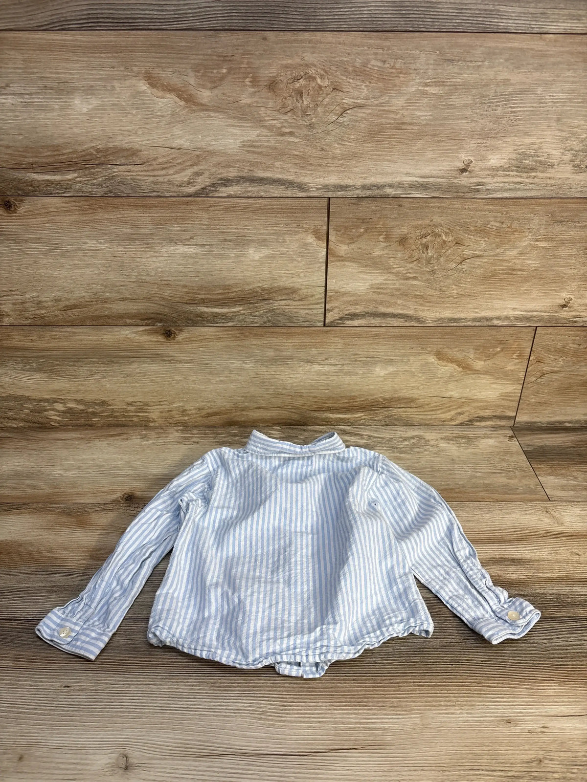 Light blue and white striped long sleeve toddler shirt on wood background