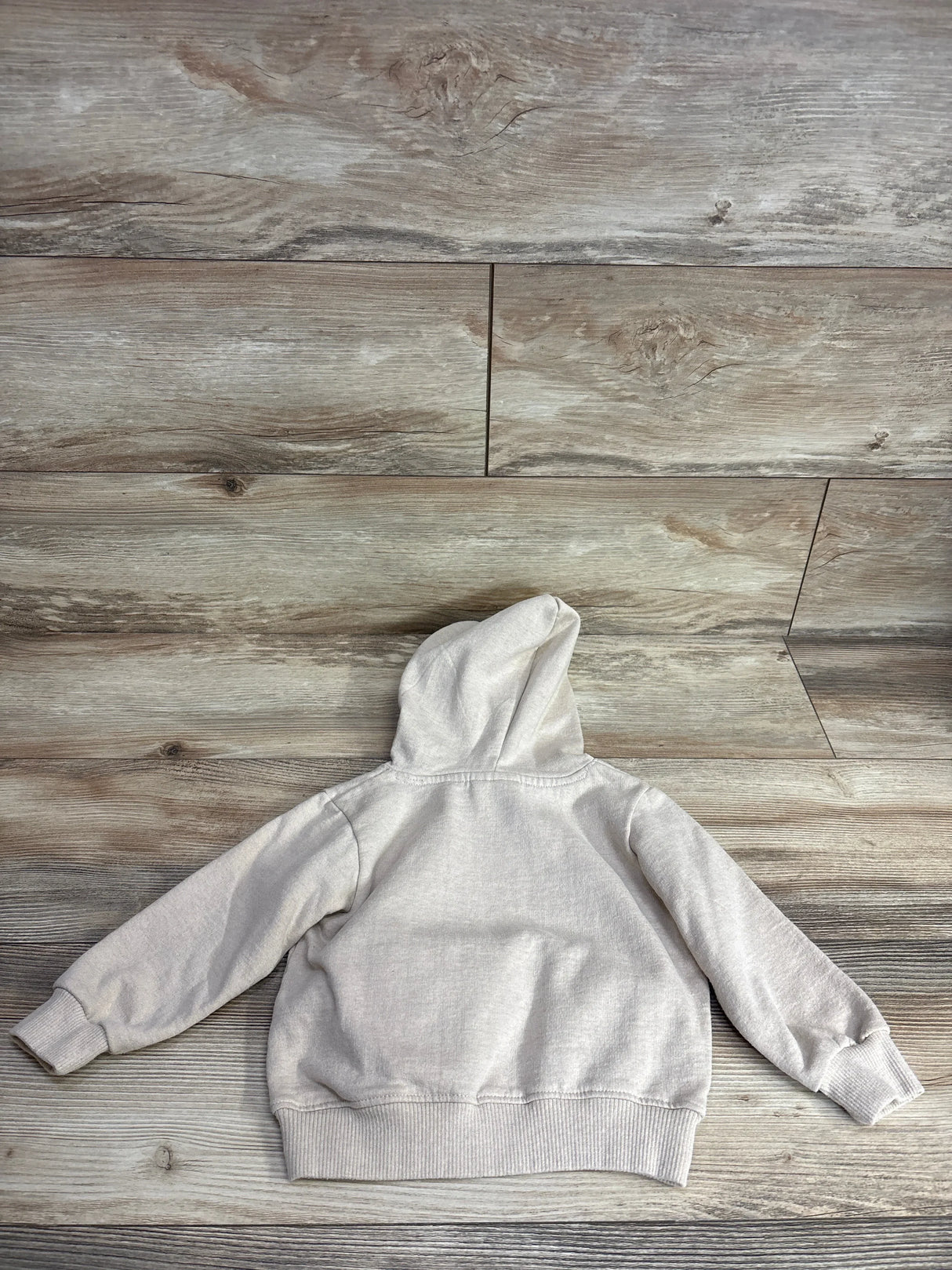 Beige kids hoodie laid flat on wood floor, long sleeves, casual children's clothing