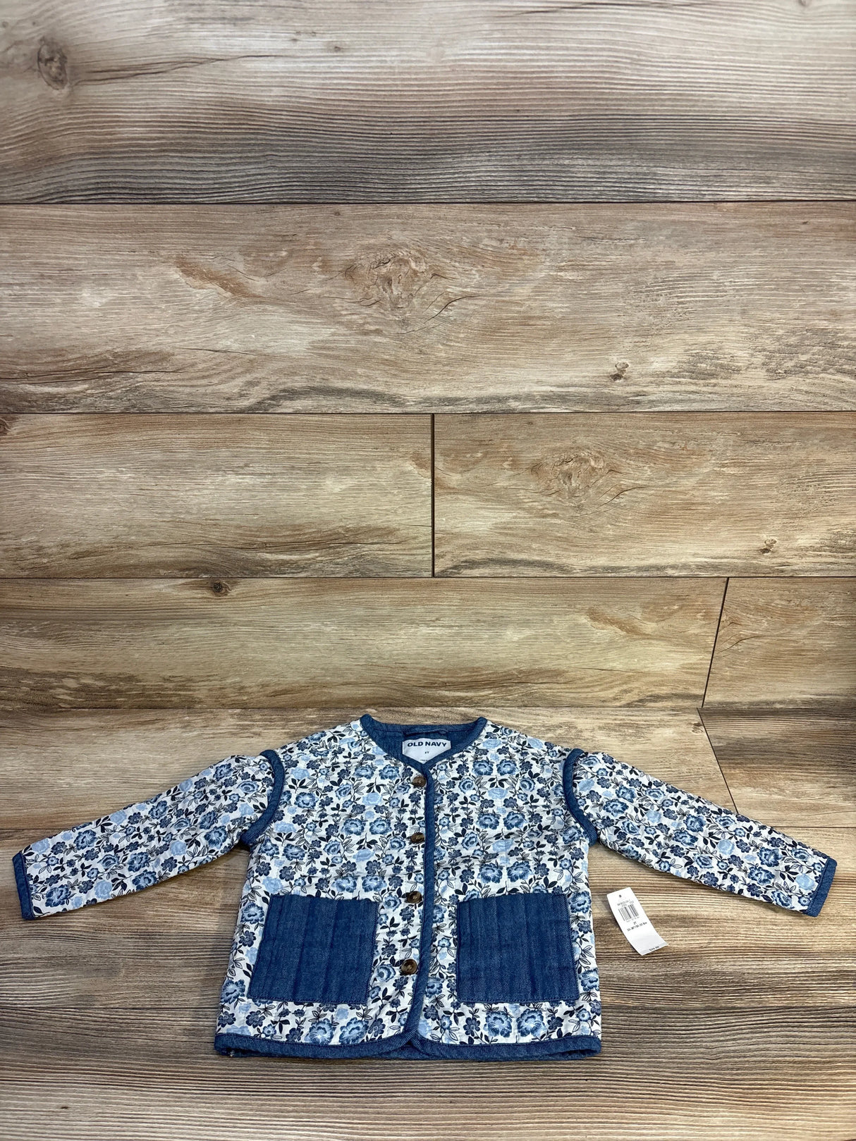Kids floral long sleeve jacket with blue denim pockets and button front on wood background