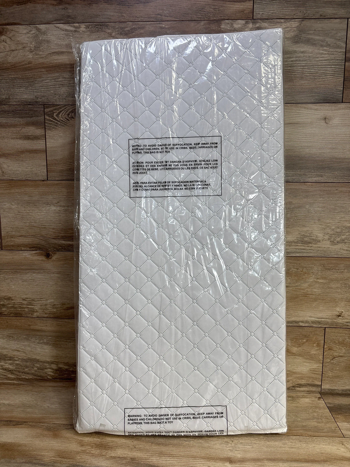 Top-down view of Dream On Me cradle mattress showcasing quilted white cover sealed in clear plastic on wood floor