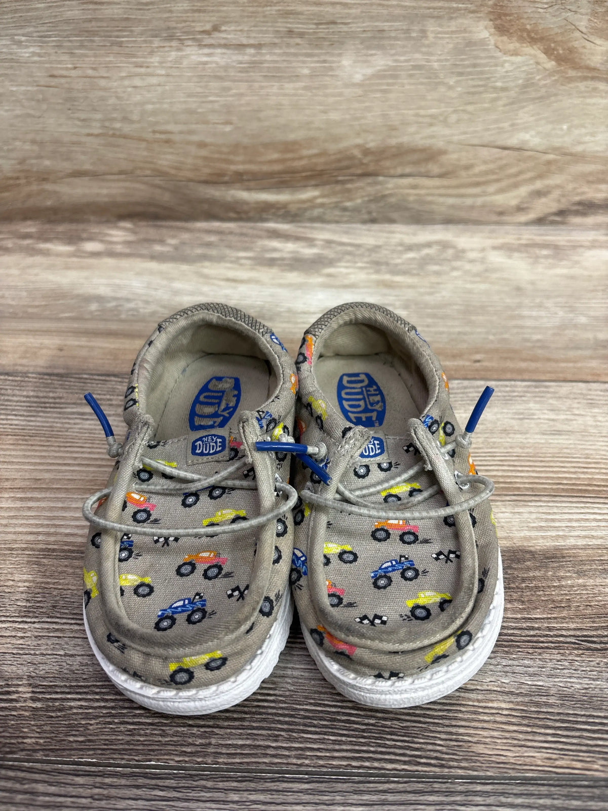 Pair of tan Hey Dude Wally T toddler shoes with colorful truck prints and blue laces.