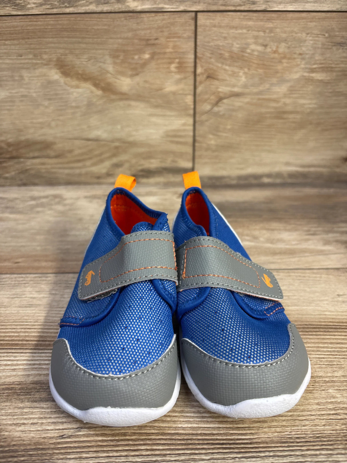 Front view of See Kai Run Ryder FlexiRun water shoes, blue with gray toe caps and Velcro straps, orange pull tabs on wood floor