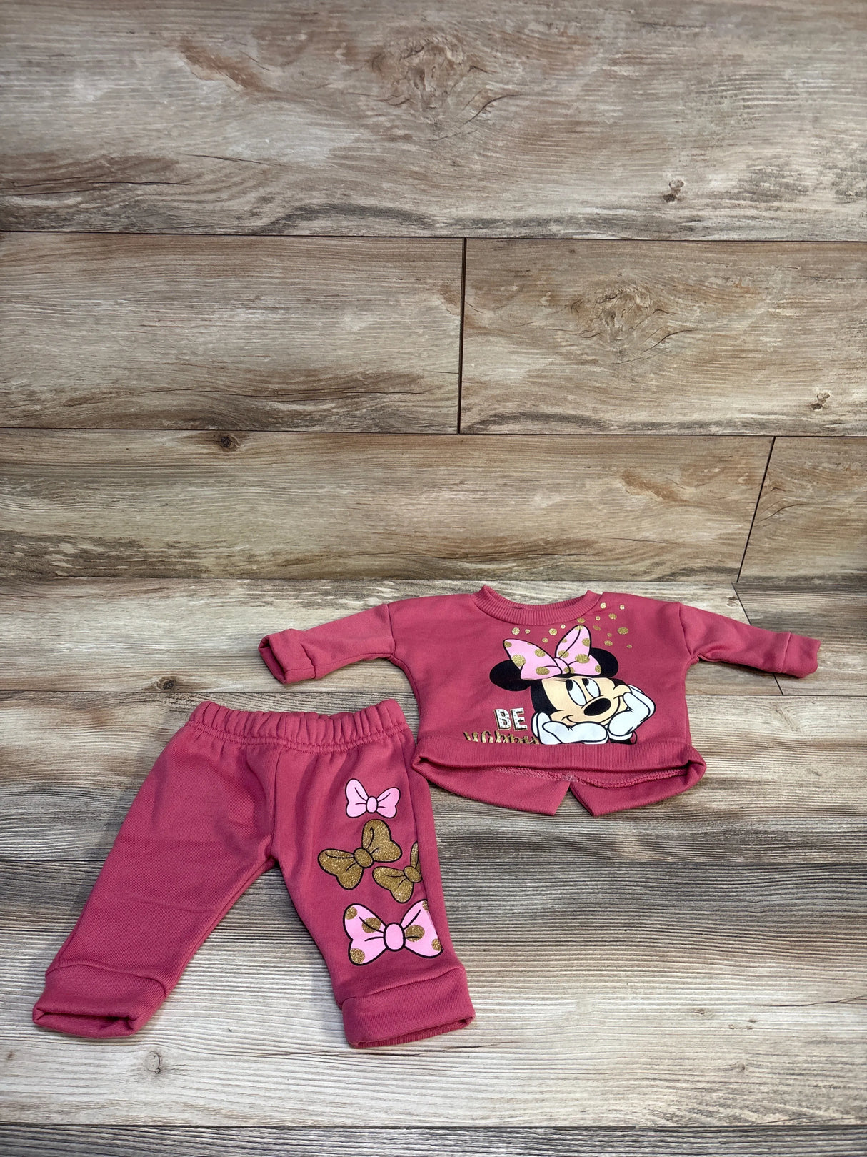 Flat lay of pink Minnie Mouse sweatshirt and joggers with Minnie graphic and bow prints on wood background