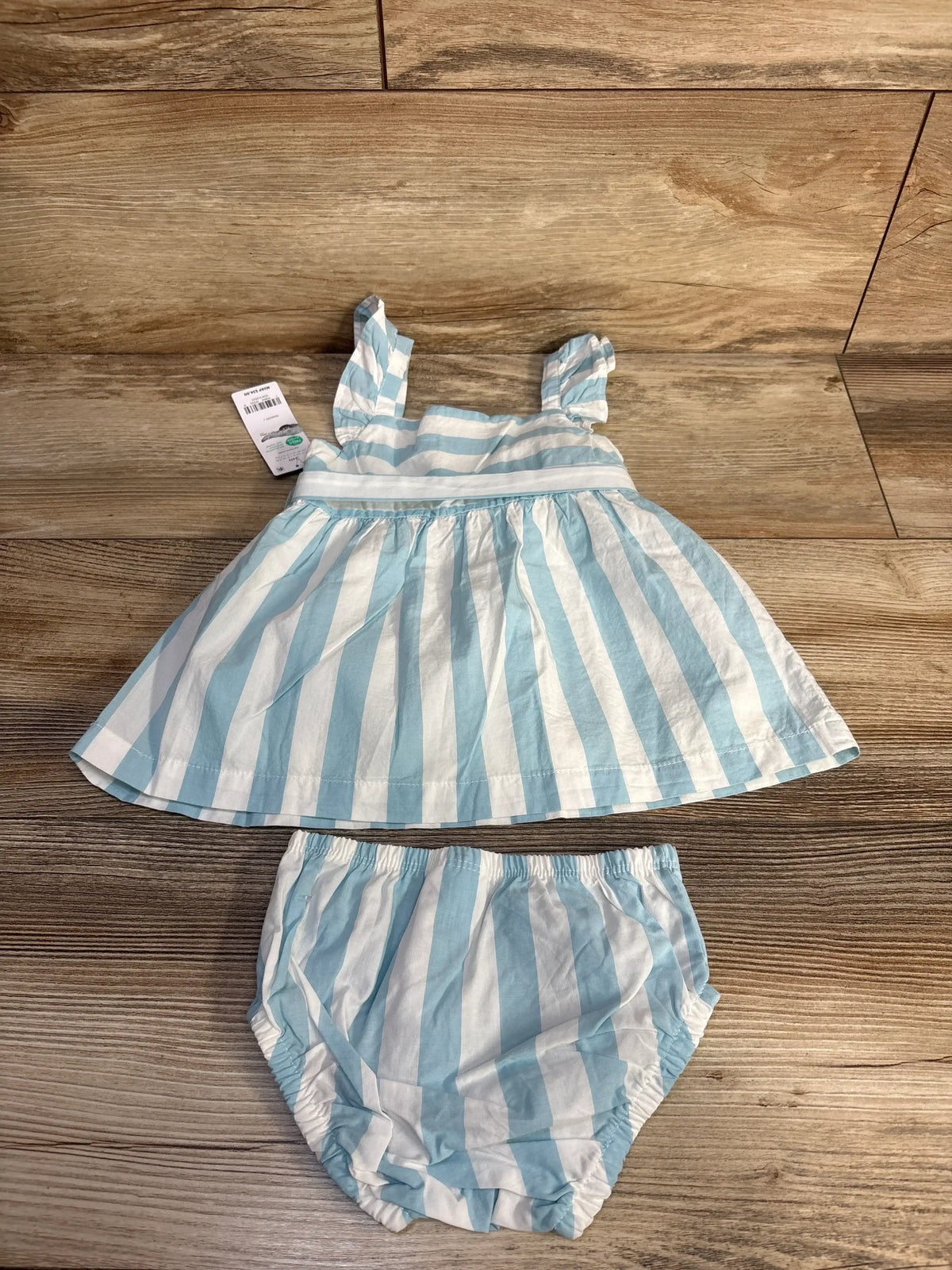 Top view of blue and white striped infant dress with ruffled straps and matching bloomers on wood background, size 3M