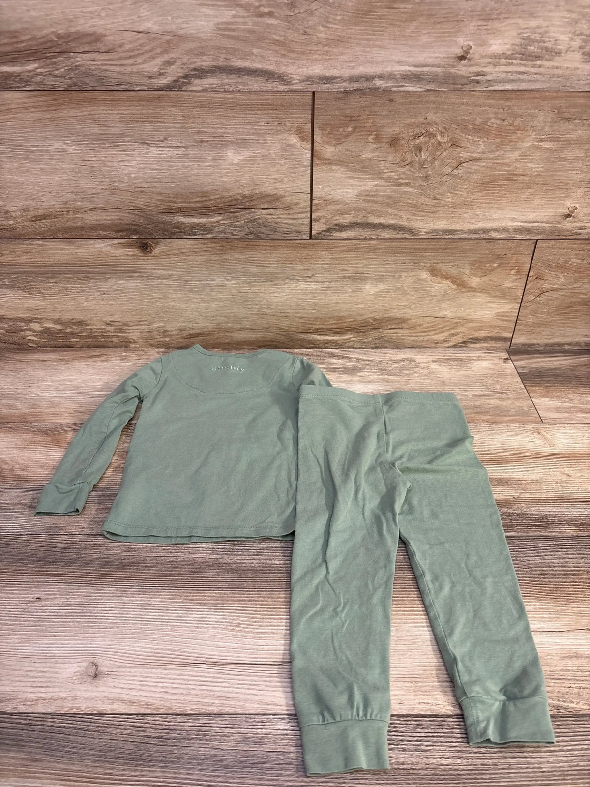 Flat lay of 2T green Magnetic Me two-piece pajama set showing long-sleeve top and cuffed ankle pants on wood background