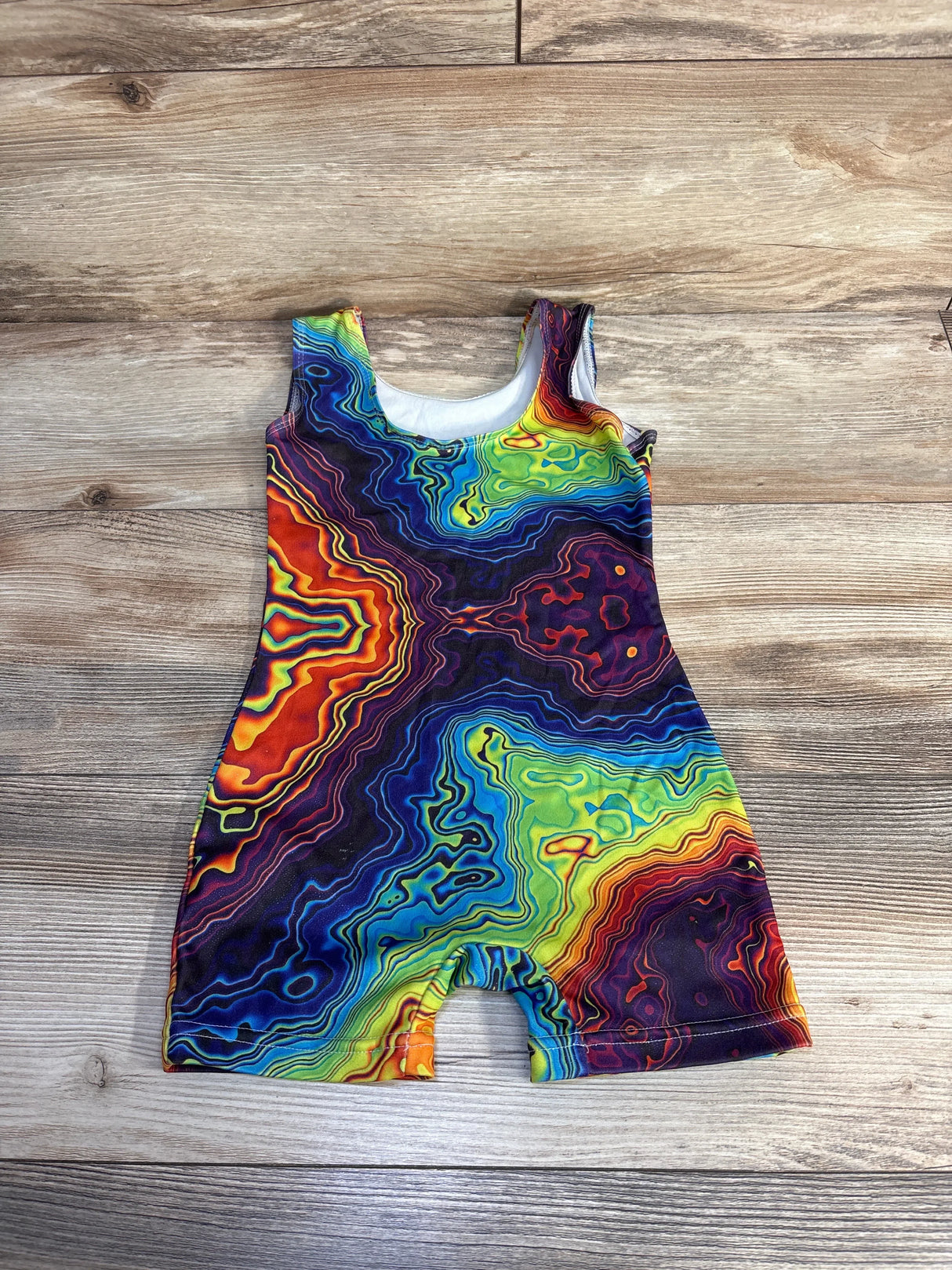 Flat lay of Biketard Thermal Print Multicolored sz 3T showcasing sleeveless one-piece with vivid rainbow topographic swirl pattern on wood plank floor
