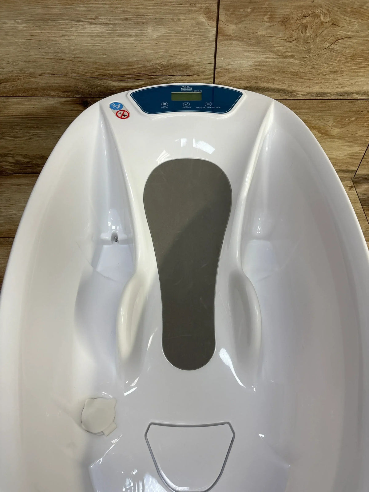 Top view of AquaScale 3-in-1 infant tub showing built-in digital scale and contoured ergonomic support on wood floor background