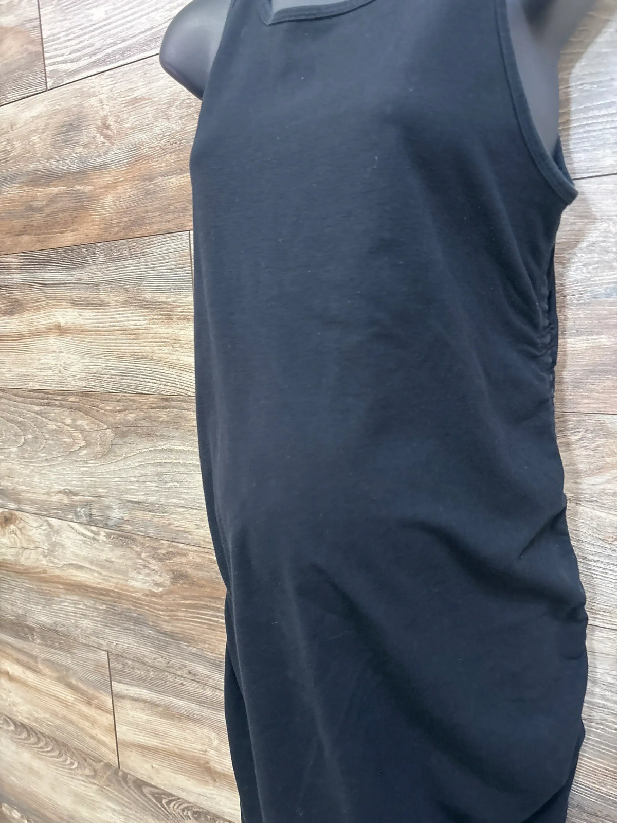 Side view of black Isabel maternity tank bodycon dress showing side ruching and fitted silhouette on wood background