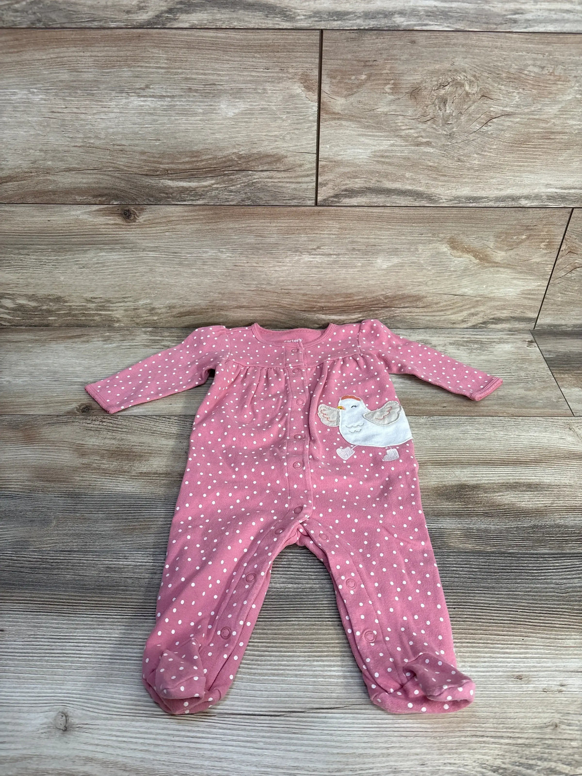 Top-down view of Carter's pink polka-dot footed snap sleeper (6m) showing front snaps and bird applique on wood background