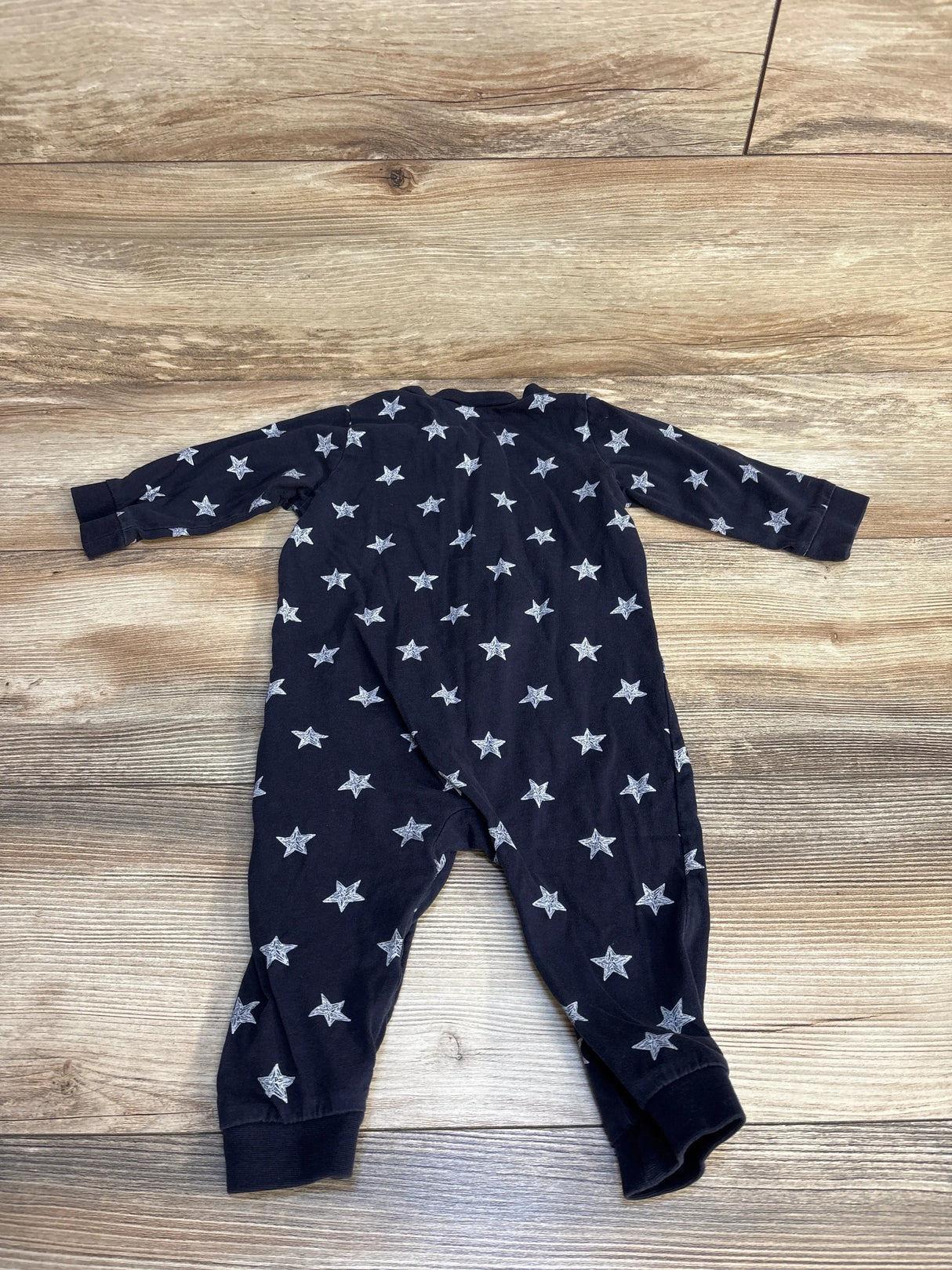 Back view of baby sleeper in black showcasing white star print with long sleeves and ribbed cuffs on wood plank floor