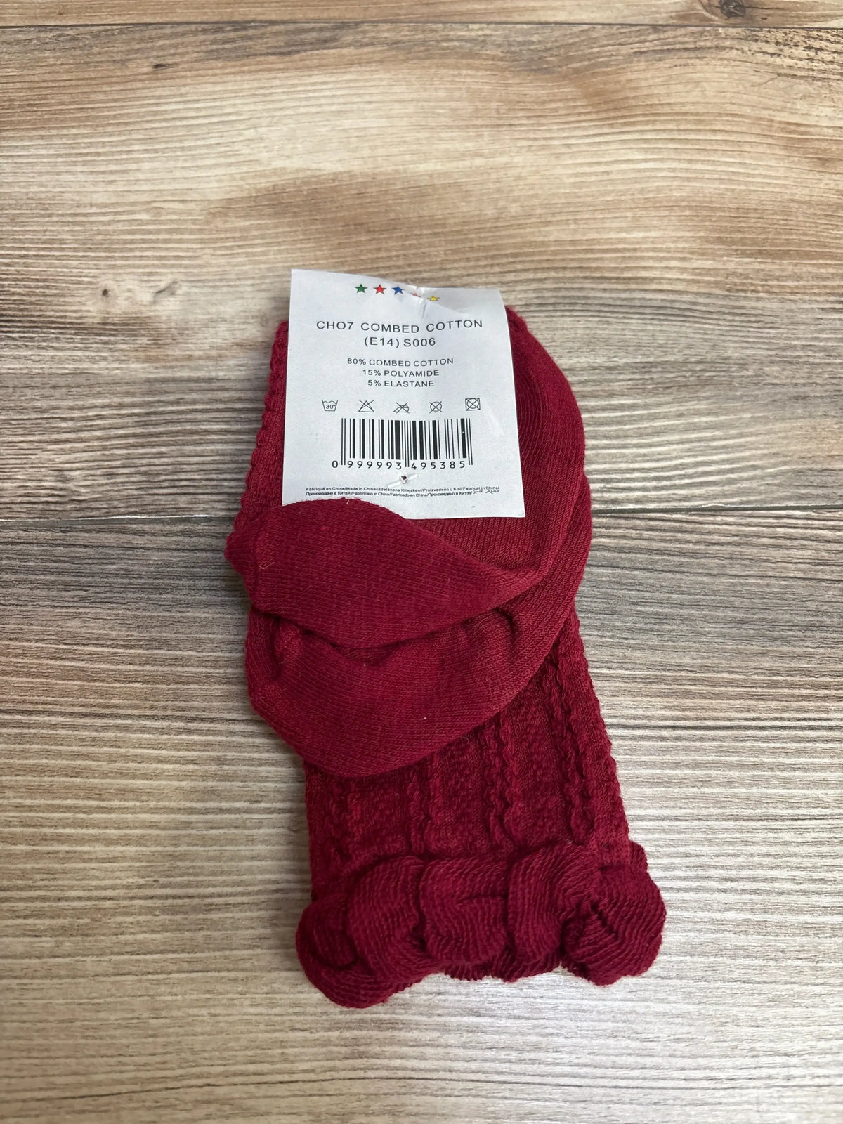 Red knitted baby socks with braided cuffs on wood surface, combed cotton blend