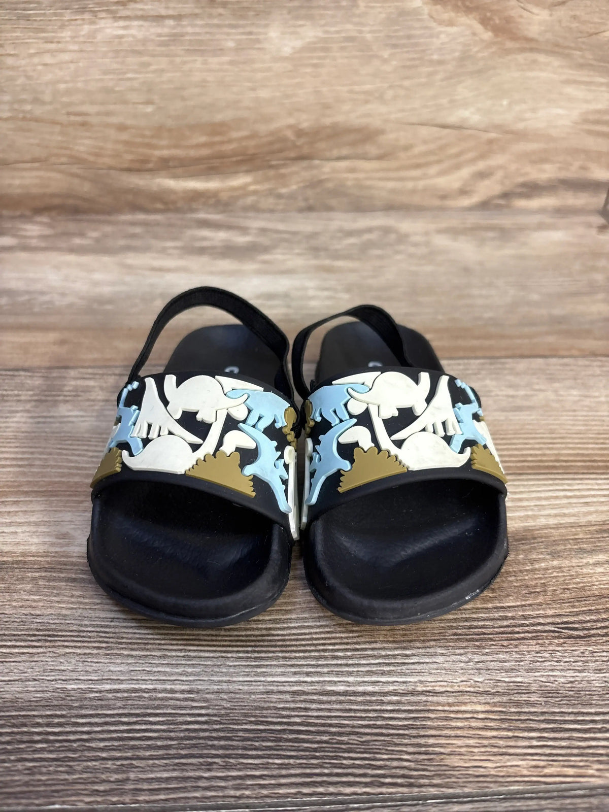Cozy Cub black dinosaur slide sandals for kids with colorful dinosaur graphics.