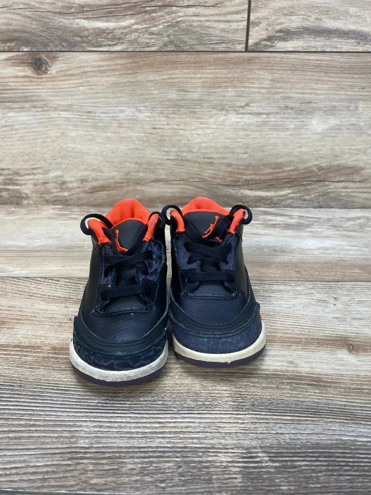 Front view of toddler Jordan 3 sneakers in black with crimson lining, Jumpman logo and elephant-print toe on wood floor