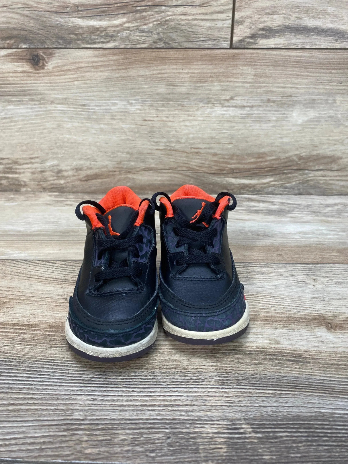 Front view of toddler Jordan 3 sneakers in black with crimson lining, Jumpman logo and elephant-print toe on wood floor
