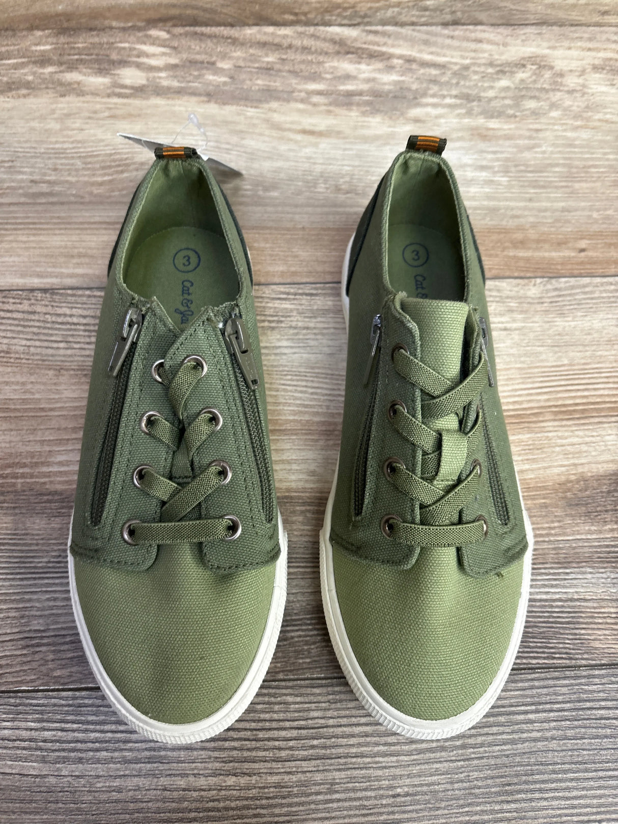 Pair of kids size 3 green canvas sneakers with side zippers and white soles on wooden floor
