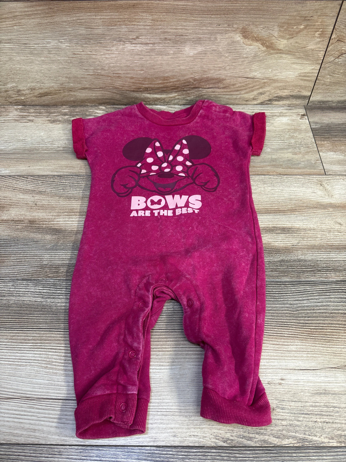 Front flat lay of pink Disney romper showcasing Minnie bow graphic and text BOWS ARE THE BEST on wood background