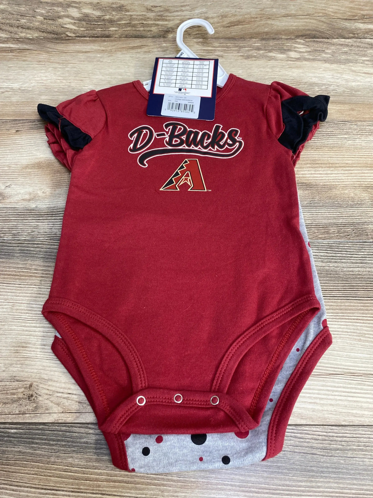 Top-down of red Arizona Diamondbacks 2-piece baby bodysuit showing D-Backs logo, snap crotch, and ruffle sleeves on wood background