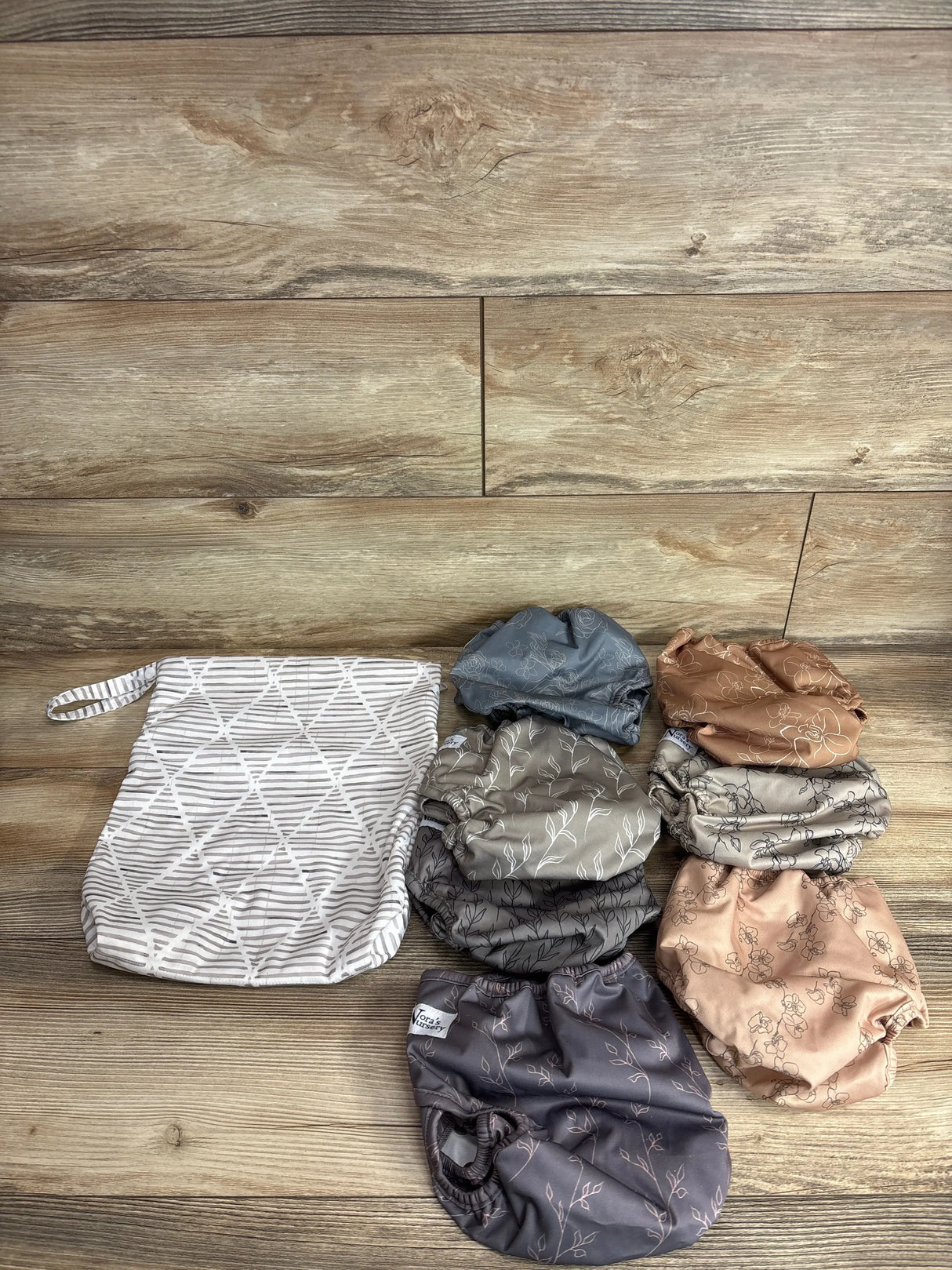 Top view of Nora’s Nursery 7pk cloth swim diaper covers and wet bag showcasing seven assorted patterns on a wood surface
