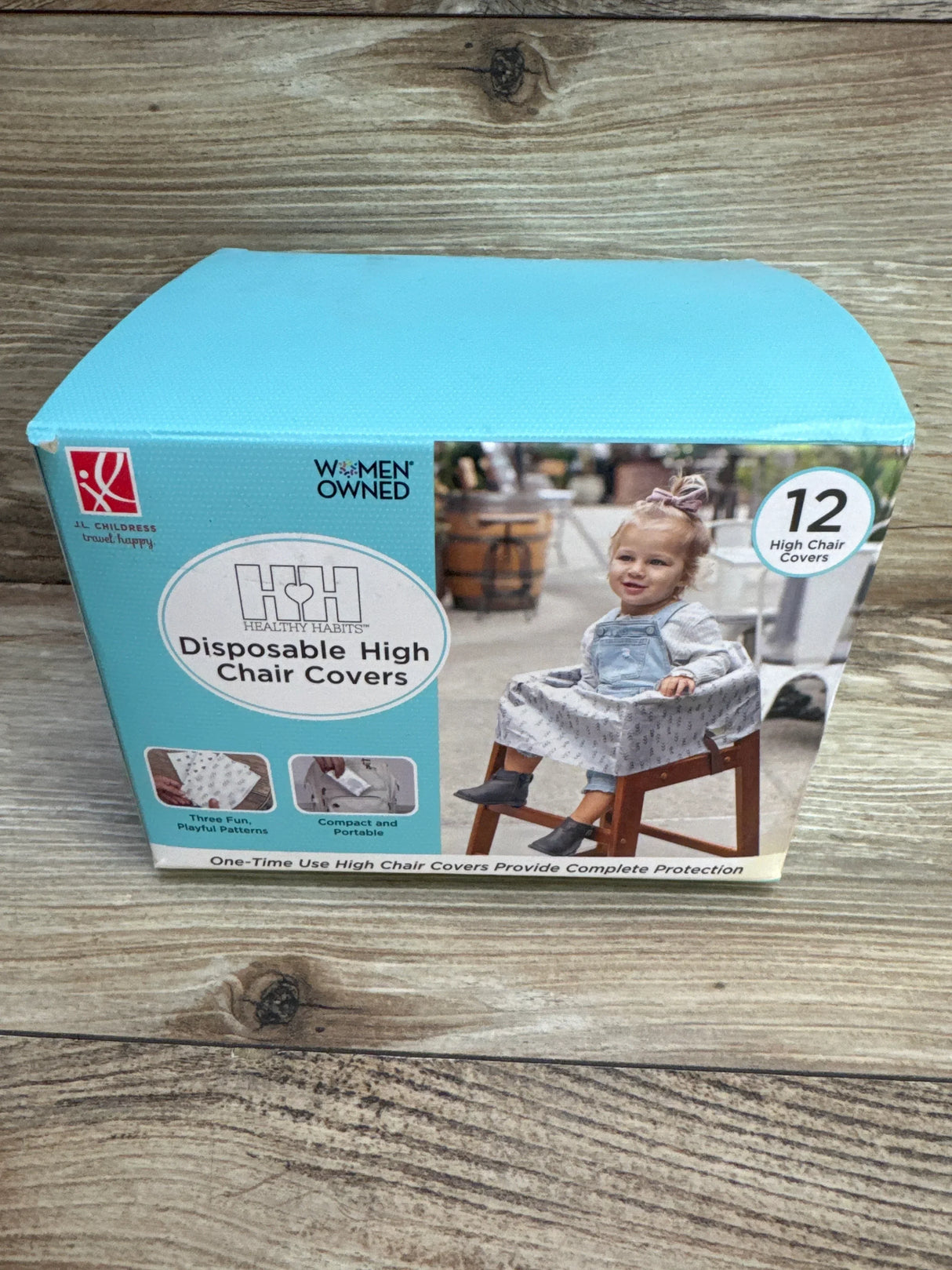 Front view of boxed J.L. Childress disposable high chair covers showing toddler photo and 12-count badge on wood background