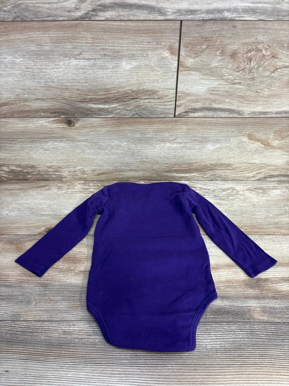 Purple long sleeve baby bodysuit on wood background