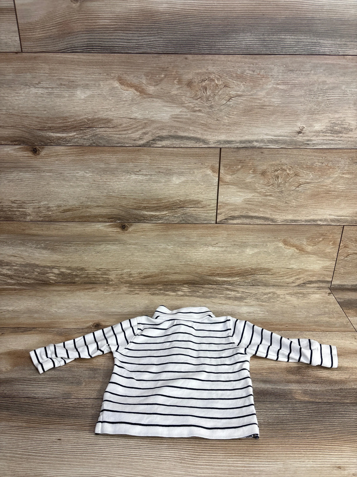 White long-sleeve toddler shirt with black horizontal stripes on wooden background