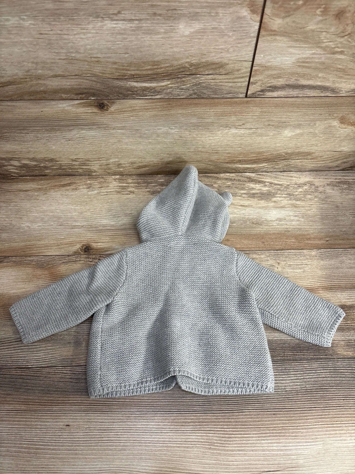 Gray knitted baby hoodie with bear ears on wooden background, infant clothing