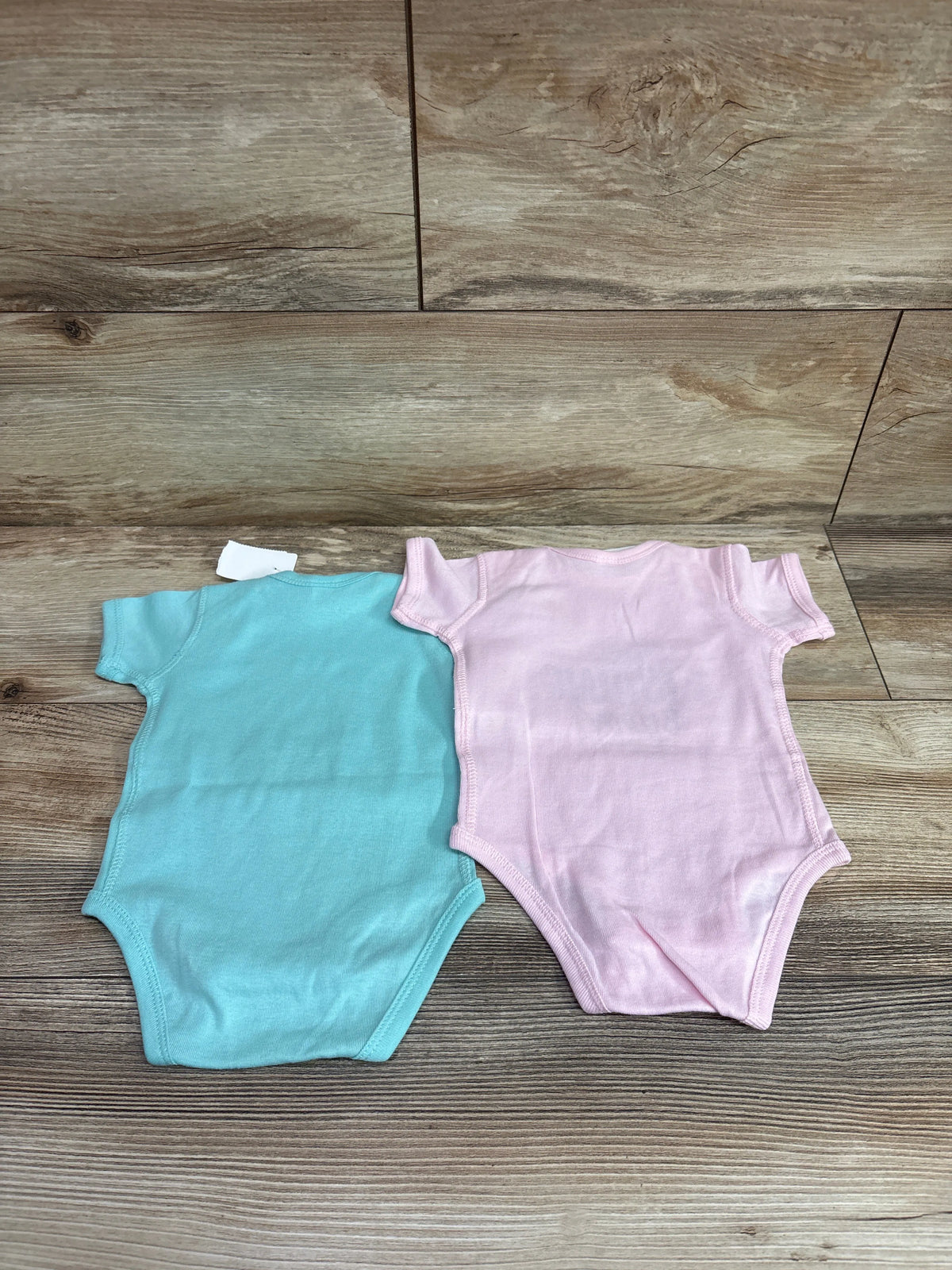 Two Rabbit Skins baby bodysuits in light blue and pink laid on a wooden background.