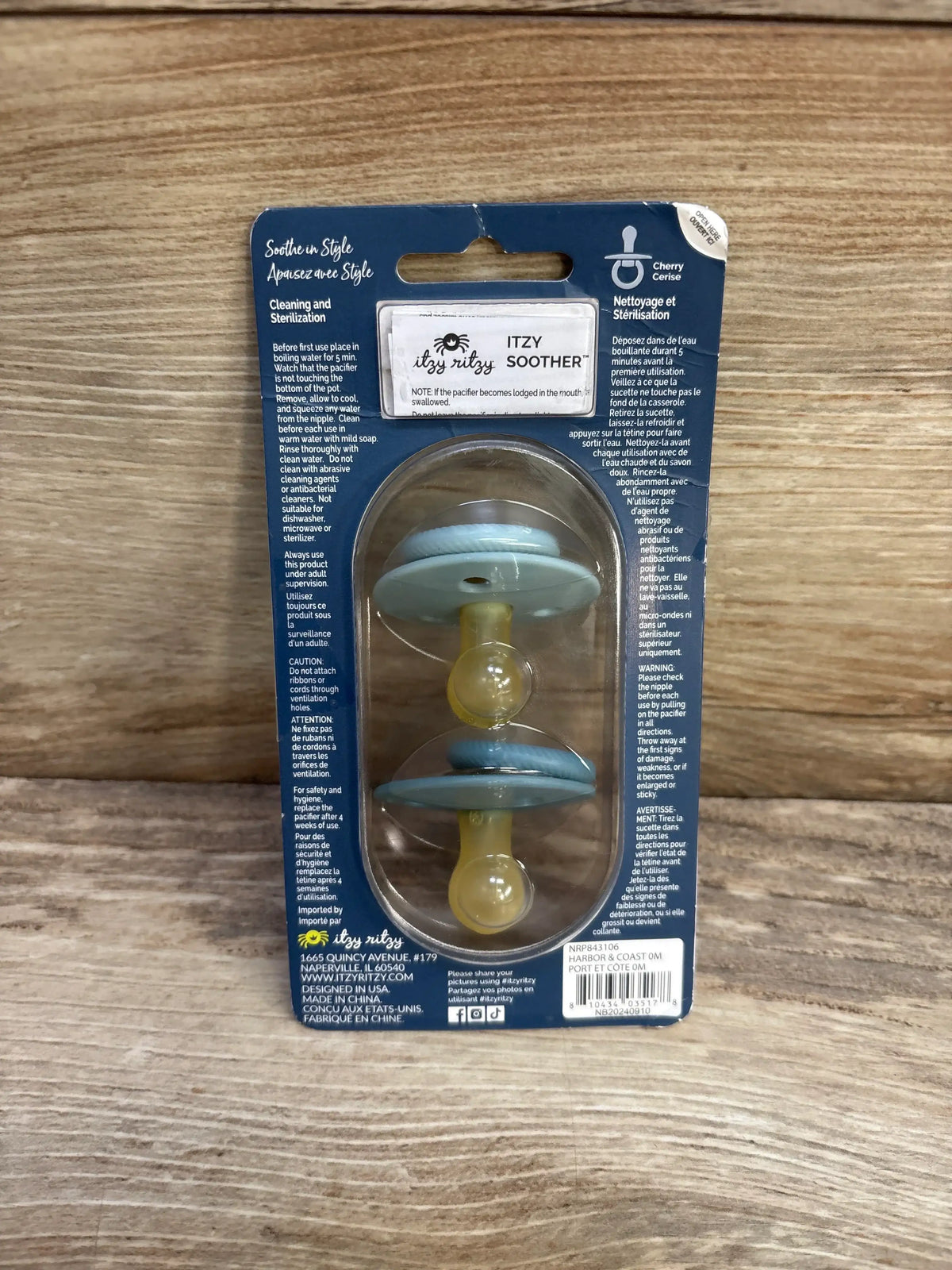 Front view of two Itzy Ritzy natural rubber soothers in Harbor and Coast packaging, blue patterned shields on wood