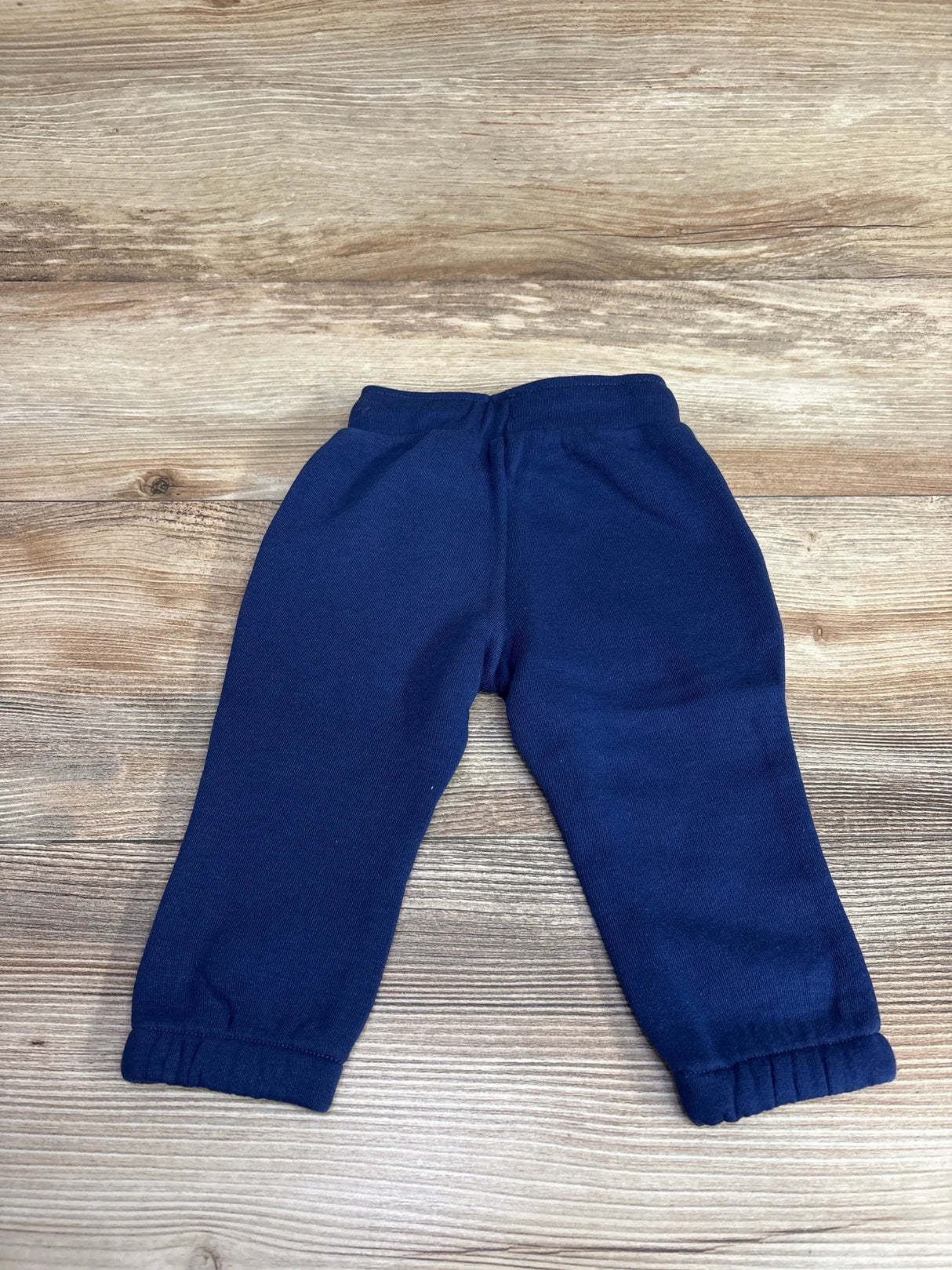 Navy blue toddler fleece sweatpants with elastic cuffs on wooden floor background