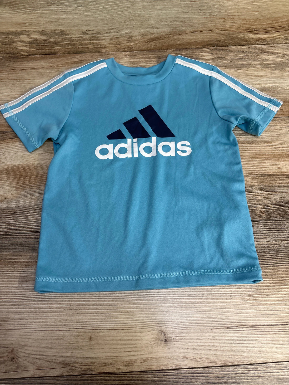 Blue Adidas kids t-shirt with white stripes and logo on wood background