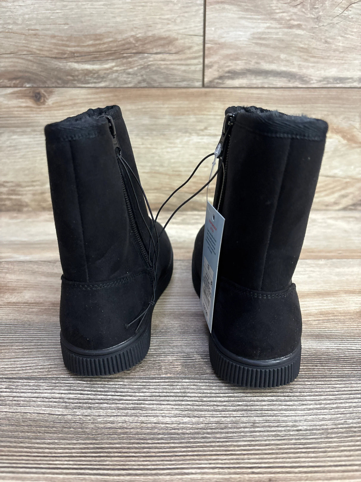 Back view of Cat & Jack Holland shearling-style kids black boots size 13C showing back zipper, faux-fur cuff and ribbed soles on wooden floor
