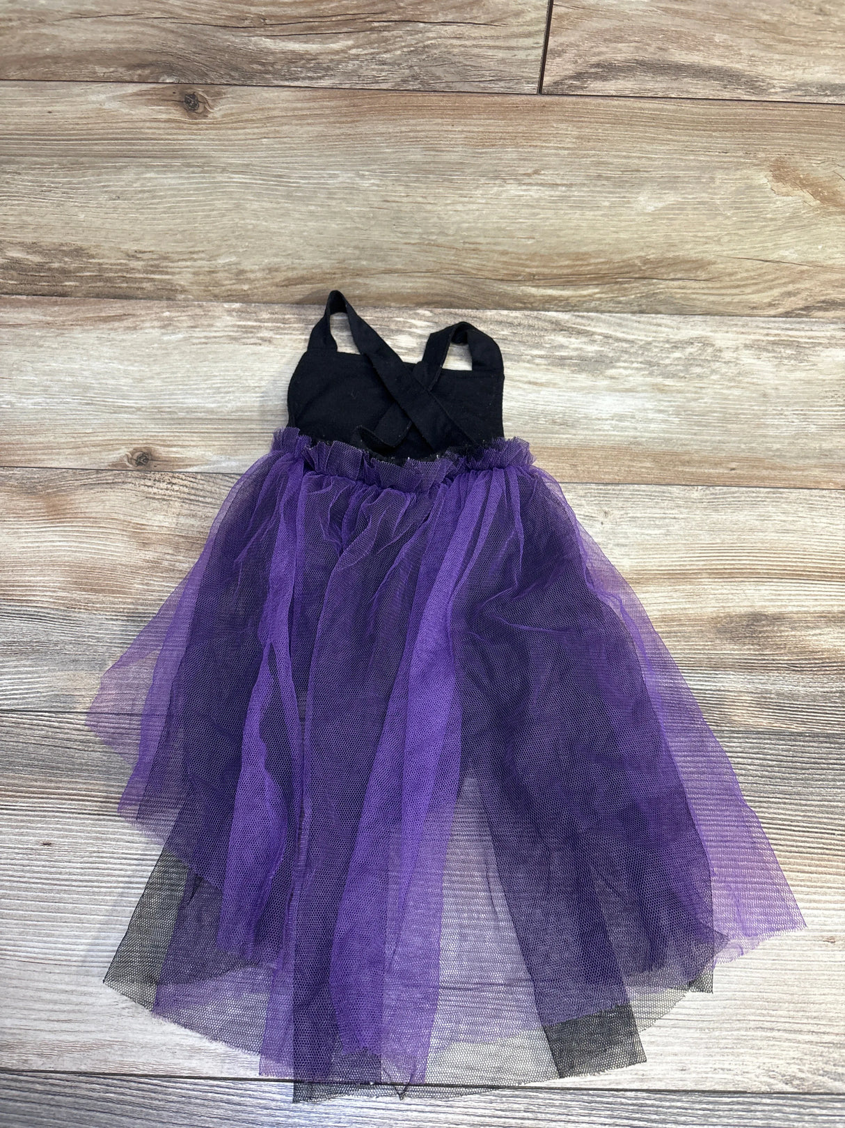 Front view of a black and purple Halloween tulle cape bubble romper laid flat on a wood-look floor