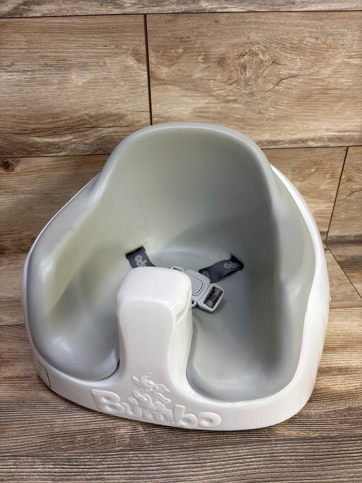 Three-quarter view of Bumbo Multi Seat showing grey inner seat, white base with embossed logo and harness on wood floor