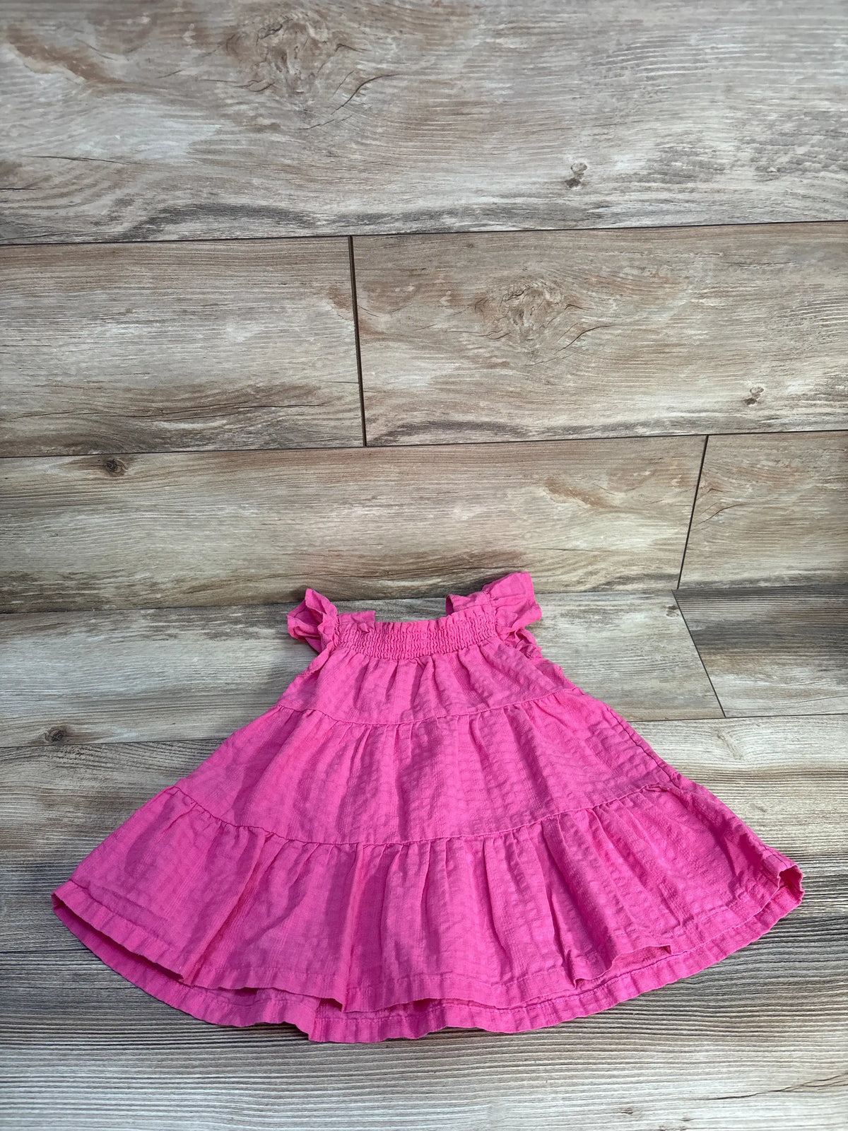 Front view of Old Navy pink smocked tiered dress, size 12 to 18 months, with smocked bodice and layered skirt on wood flooring