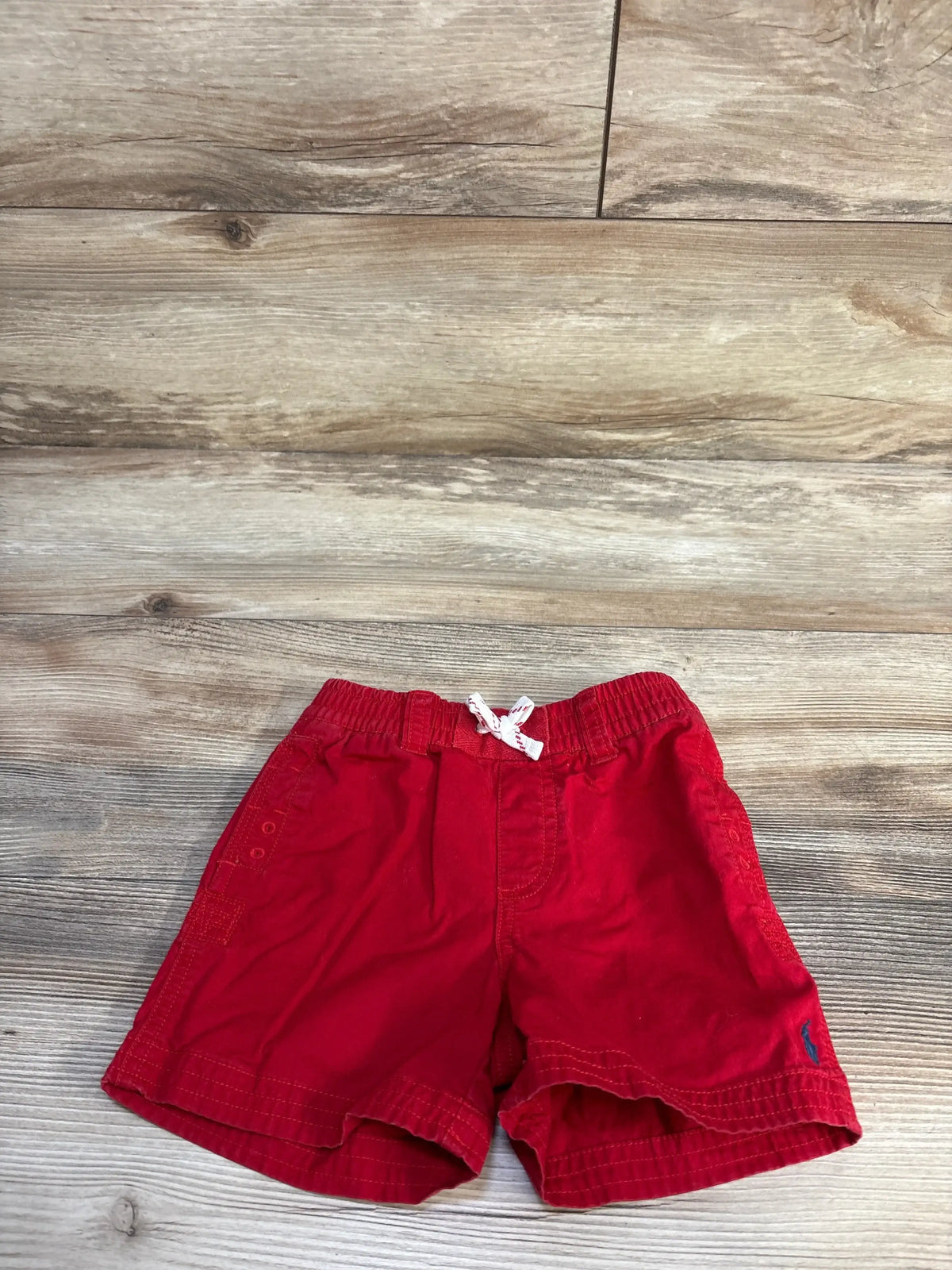 Front view of red Ralph Lauren baby shorts with drawstring elastic waist and embroidered pony on wood floor background