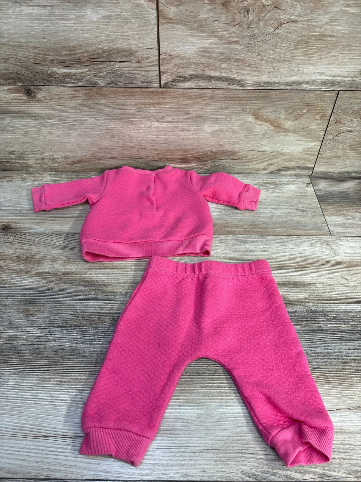 Flat lay of two piece quilted baby sweatshirt and pants in pink showing textured quilting and ribbed cuffs on wood floor