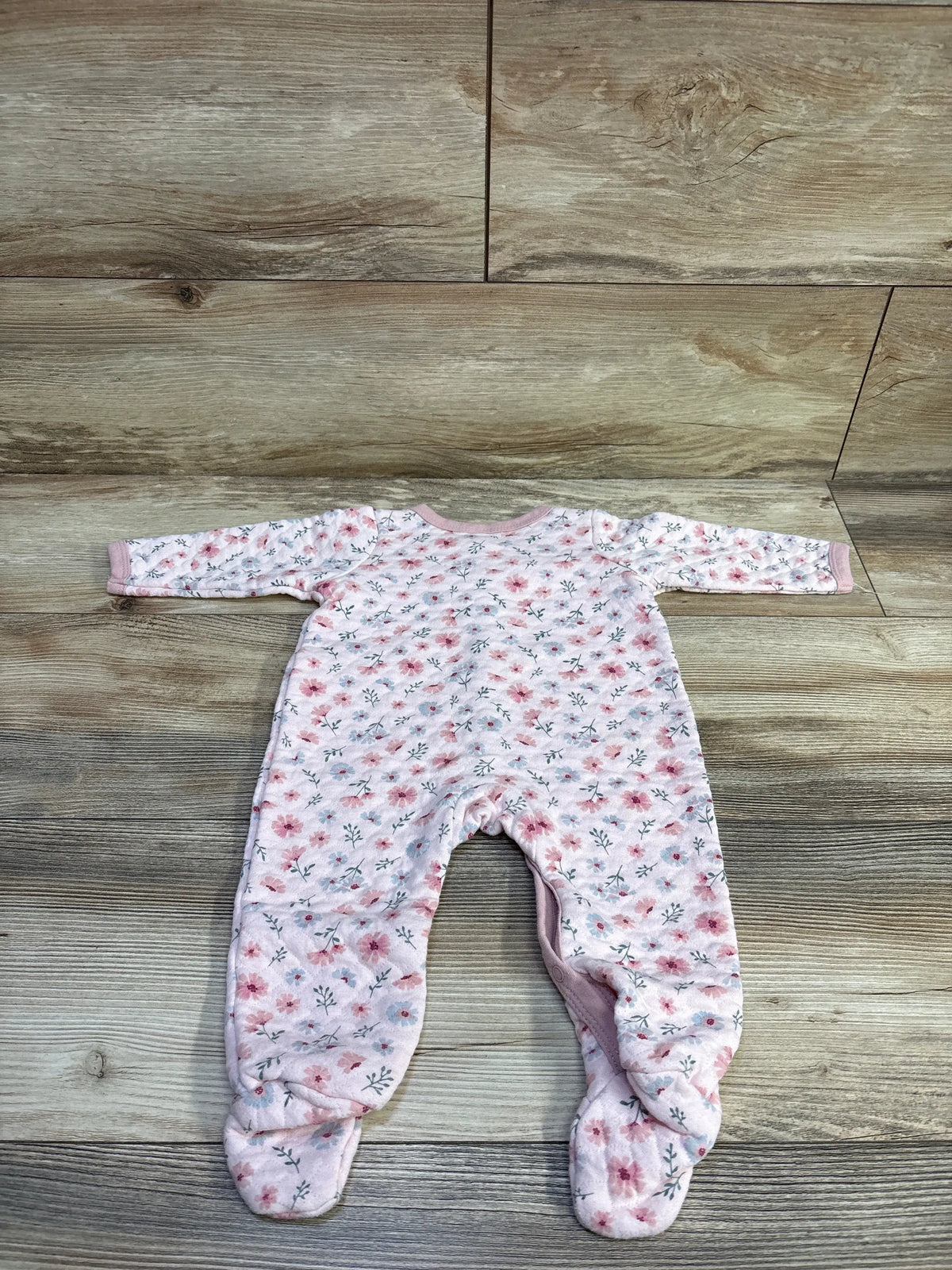 Flat lay of quilted pink floral footed sleeper size 6-9 months showing long sleeves and attached feet on wood floor